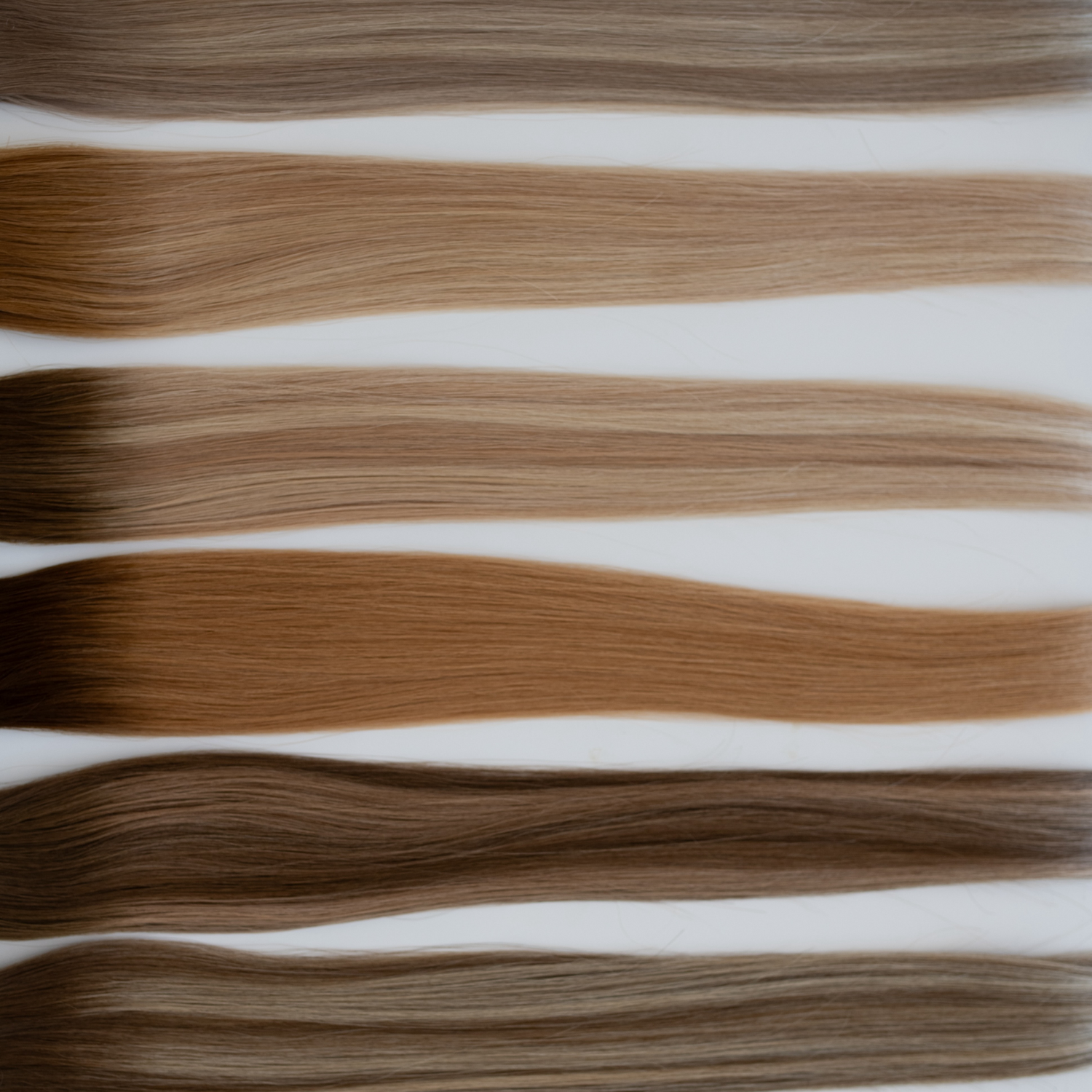Assorted Siren Luxury Hair Extensions in various shades, displayed in a horizontal layout to showcase the smooth texture and premium quality of Remy Human Hair. Includes a range of blonde and brunette tones.